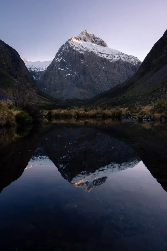 Mount Talbot reflected in a still body of water and framed by two other mountains at sunrise