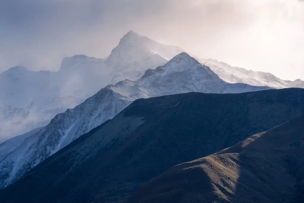 Mountain peaks at Lake Pukaki in mist and golden light covered in snow