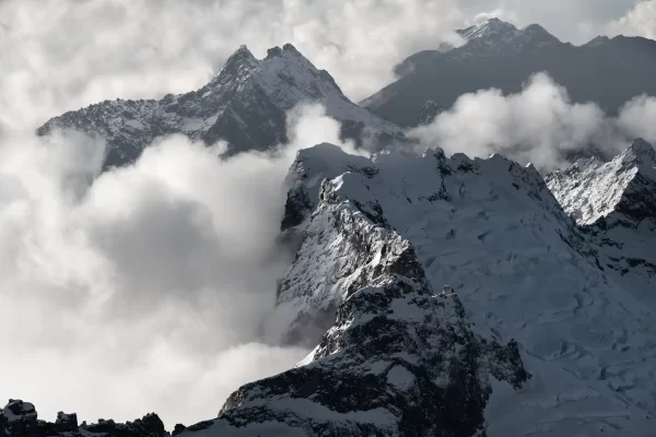 Black and White aerial photo of multiple mountains covered in snow and surrounded by cloud in New Zealand