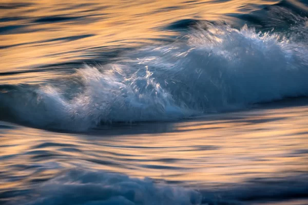 Long exposure photo of waves at sunset with yellow and orange reflections on the water