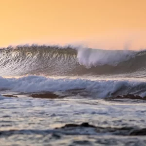 Large waves breaking at sunrise with an orange sky