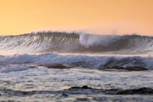 Large waves breaking at sunrise with an orange sky