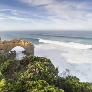 The Arch with waves breaking on the coast with blue skies and green coastal flowers