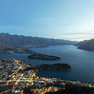 Aerial shot of Queenstown during blue hour with the city lit up and the remarkable mountains behind