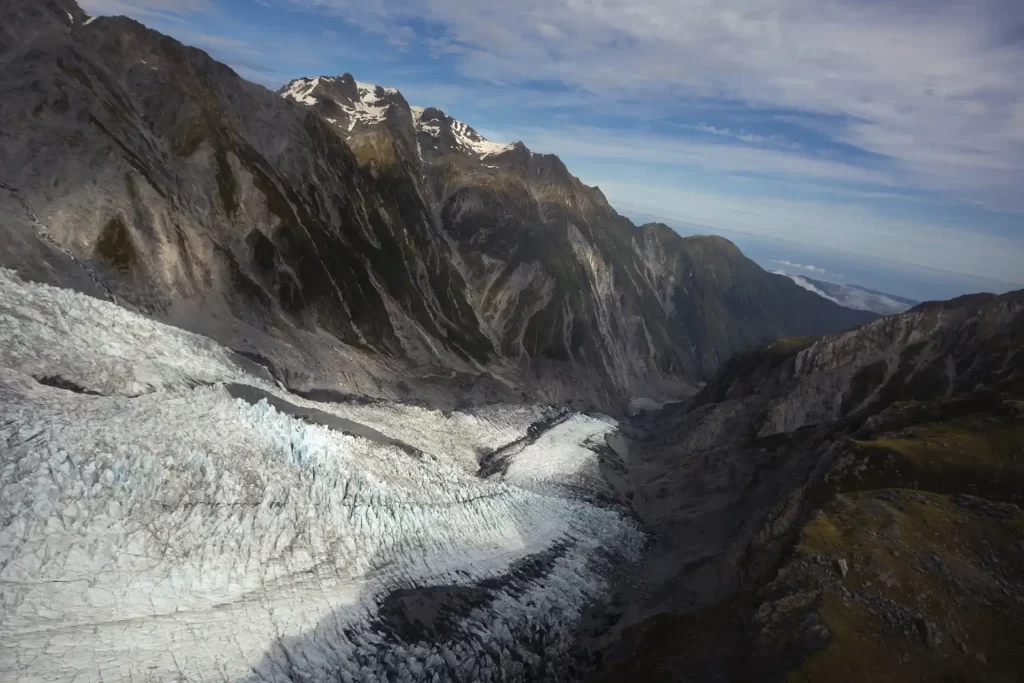 Aerial view looking down Franz Josef with blue skies and mountains surrounding