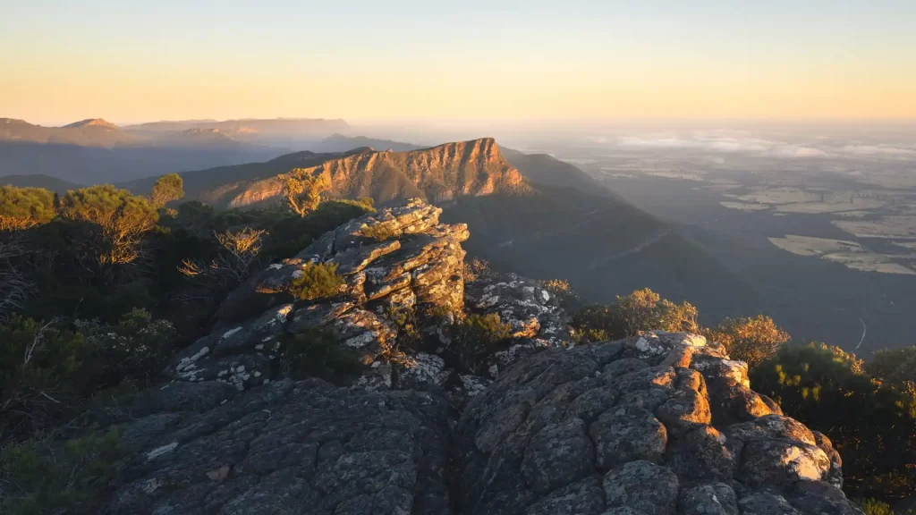 View from Mount William overlooking mountains in the Grampians with a yellow and orange sunrise