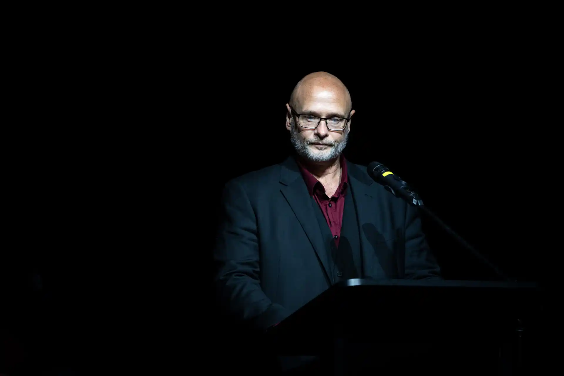 A corporate photo of a presenter on a dark stage speaking